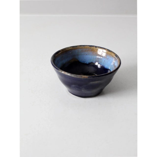 A vintage studio pottery bowl signed by the artist, Margo. The handcrafted ceramic bowl features a layered glaze in navy...