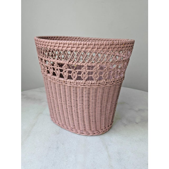 A vintage wastebasket in pink woven wicker design.