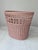 A vintage wastebasket in pink woven wicker design.