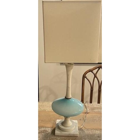 An elegant Italian Mid-Century Modern table lamp featuring a vibrant turquoise-blue glass body mounted on a square marble...
