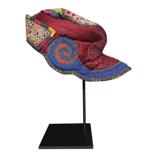A silk hat from the Miao people of China with bright colors and intricate embroidery. Displayed on a custom stand.