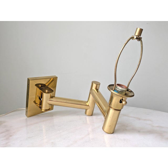 A vintage polished brass wall-mounted plug-in lamp. The lamp has an articulated adjustable arm and includes orignal brass...