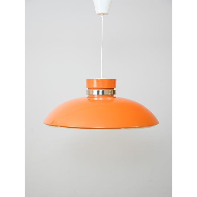 1960s-style pendant lamp in orange plastic with a ring-shaped metal insert and an integrated diffuser with concentric...