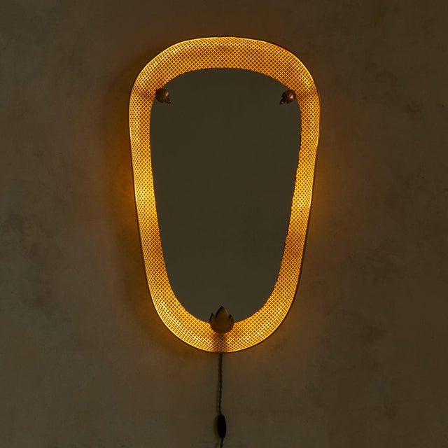 A 1950s French illuminated wall mirror attributed to Mathieu Matégot for Artimeta. The curved frame, crafted from...