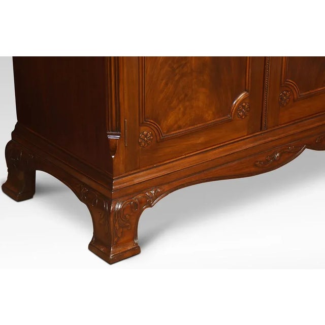 Mahogany three-door wardrobe, the moulded scrolling cornice above three long well figured panelled mahogany doors, opening...