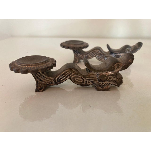 A pair of antique small iron dragon-form Chinese chop stick supports or rest with a curling serpentine body, stylized...