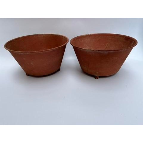 A matching pair of round tole bowls or cachepot featuring a terracotta style finish and three ball feet.