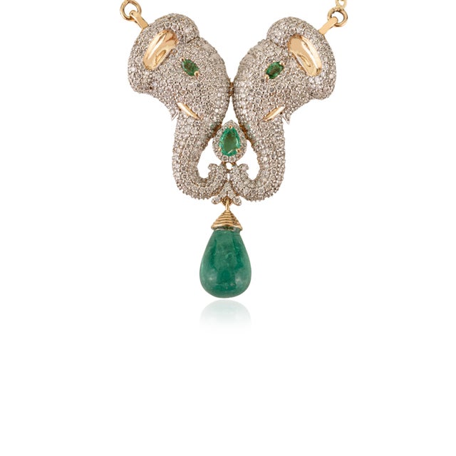 This elegant 14K yellow gold necklace features two diamond-studded elephant heads with emerald eyes, symbolizing strength...