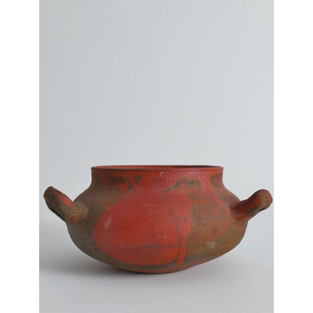This striking hand-thrown earthenware vessel features an unusual three-handled form and a richly textured surface that...