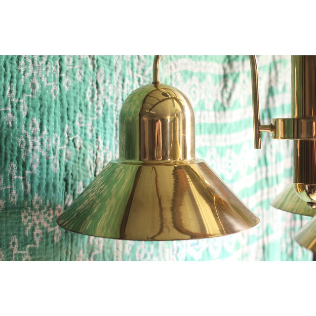 A wonderful golden brass chandelier with 3 lights and shades. Hangs from a chain to the ceiling cap. Unique form to the...