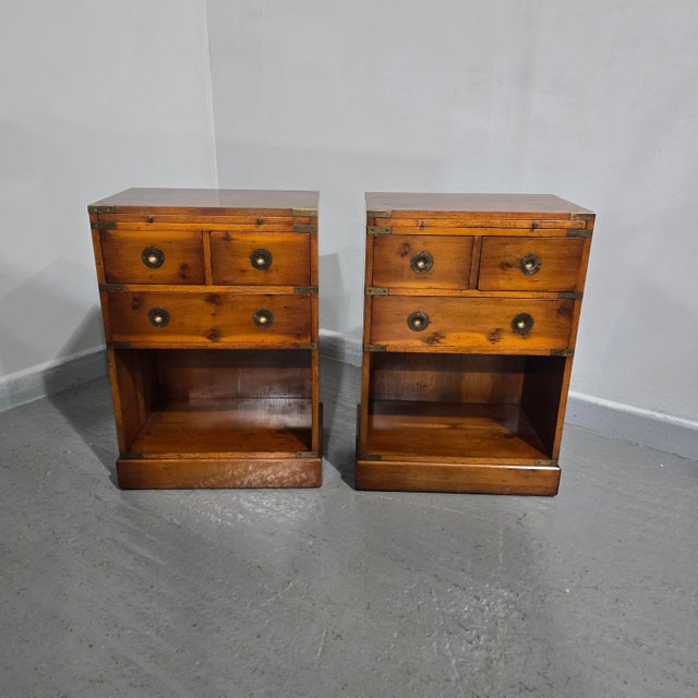 A very nice pair of yew wood three drawer campaign bedside lamp tables with green leather slide, inset brass straps and...