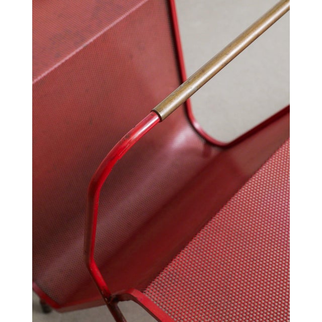 A rare french mid century modern magazine rack in red lacquered p erforated sheet metal with brass feet and handle...