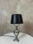 Superb silver-plated metal table lamp, finely crafted in a classic and refined style. Its tripod base adorned with ram...