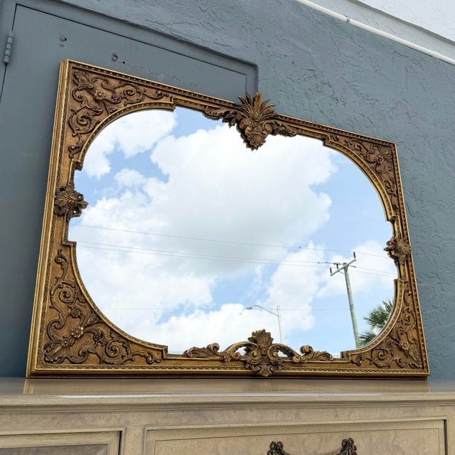 An exceptional vintage Rococo-style wall mirror featuring an intricately carved solid wood frame finished in rich antiqued...