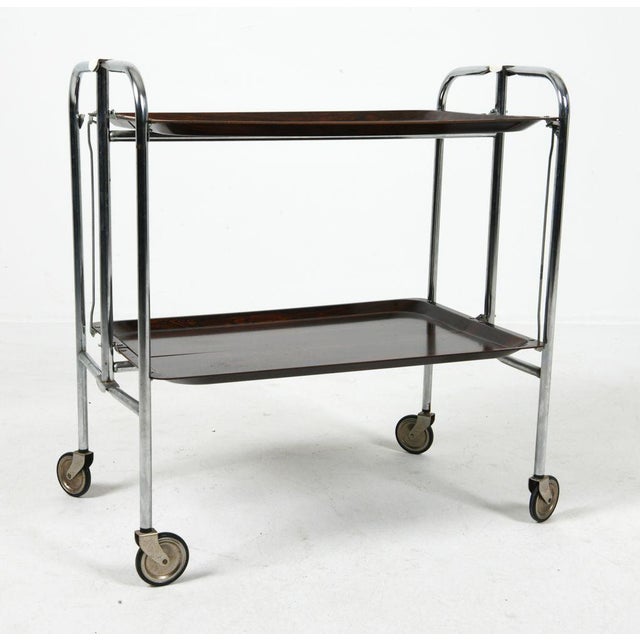 This bar cart has a chromed steel frame with plastic trays and folds up completely. While the piece is unmarked, likely...