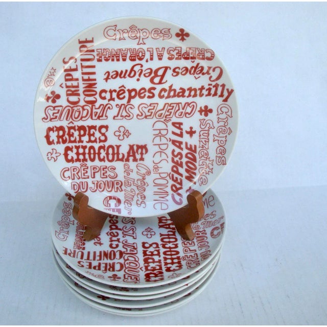 Fun graphic set of seven white and red small plates, decorated with the names of French crepe culinary delights. Circa...