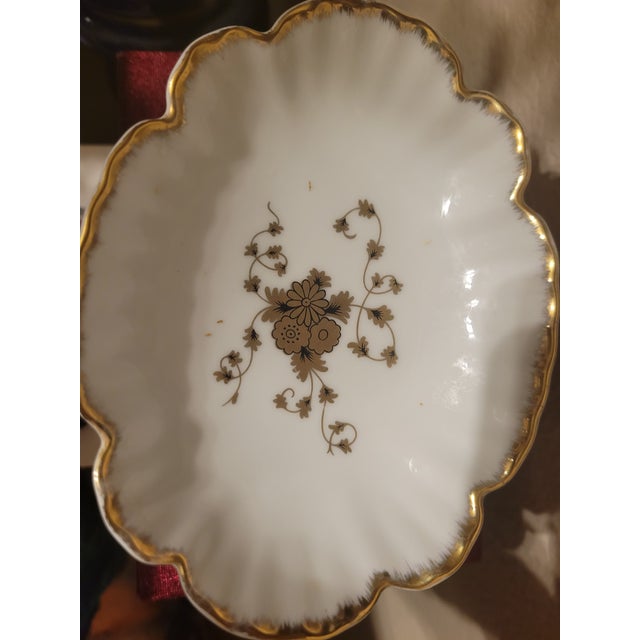 Vintage elegant porcelain pedestal soap dish featuring a scalloped rim, hand‑applied gold trim, and a central gold floral...