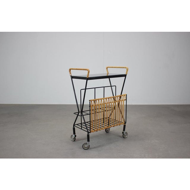 Elegant mid-century rolling magazine rack cart produced in Czechoslovakia in the 1970s. The cart features a black metal...