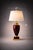 A striking Hollywood Regency table lamp featuring a deep burgundy metal urn body with polished brass accents and dramatic...