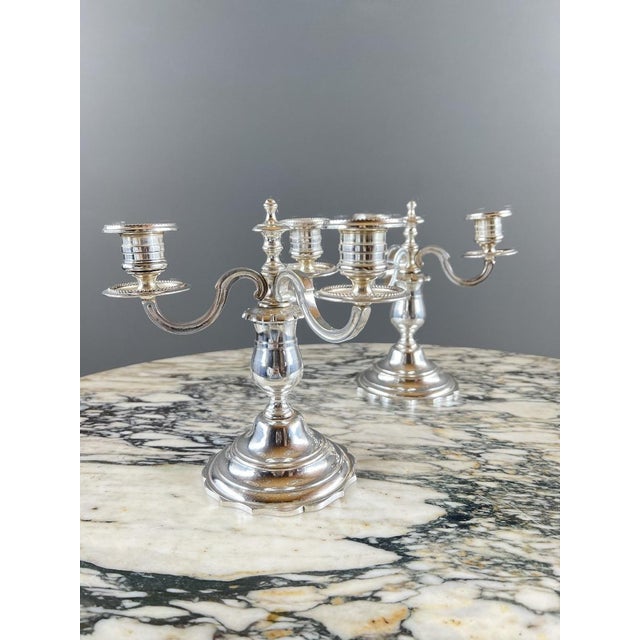 Elegant pair of three-light, silver-plated metal candelabra, resting on a baluster base with a scalloped edge. The...