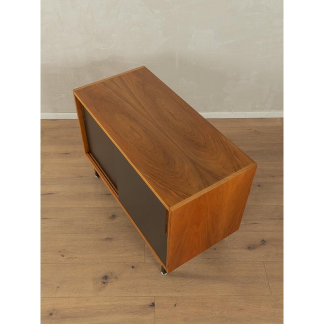 A wonderful sideboard from the 1950s. The body is made of teak veneer with two cabinet doors, four shelves, and new black...