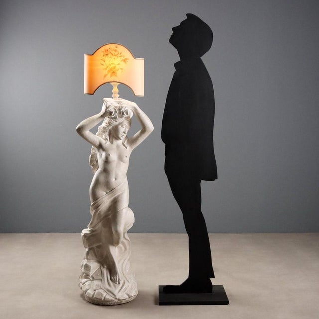 A single-light floor lamp, featuring a base composed of a Nereid statue in cement paste. The female figure, a reference to...