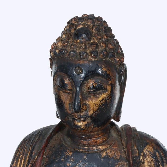 An antique carved wood seated Buddha statue, originating from the 19th century, features an ebonized finish with extensive...