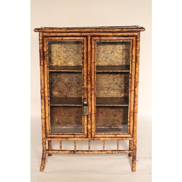 Aesthetic movement bamboo and lacquer bookcase, circa 1910. with a black lacquer top with red floral decoration, two glass...