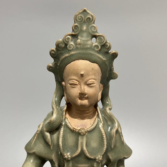 A vintage‑style Chinese Longquan celadon Guanyin statue in a relaxed seated pose. Detailed headdress and flowing carved...