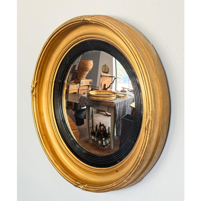 A fine English round or circular convex mirror from the Regency era, with a moulded gilt and ebonized frame.- the mirrored...