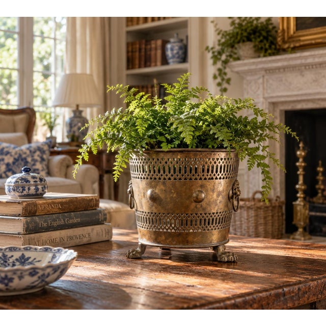 A handsome circa 1940s brass cachepot with classical lion-head ring handles, sculptural paw feet, and beautifully pierced...