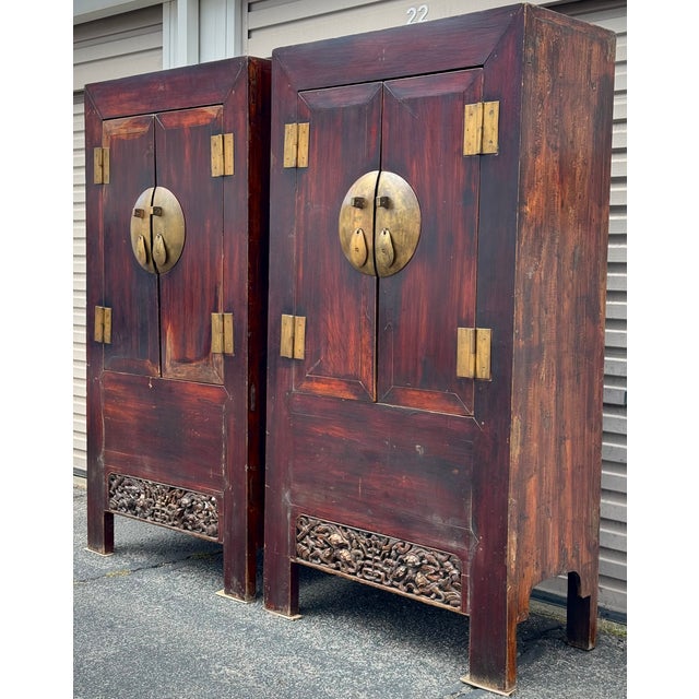 A pair of massive wooden two-door cabinets. The scale is accentuated by oversized round bronze escutcheons and pulls. The...