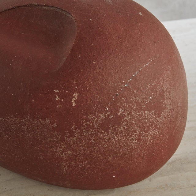 An Abstract, organic form terracotta clay sculpture featuring a smooth, red surface with natural aged patina. Delicately...
