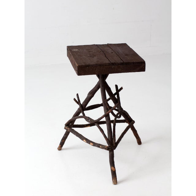 Early 20th century Adirondack twig side table featuring a handcrafted branch base and plank wood top. The intricate...
