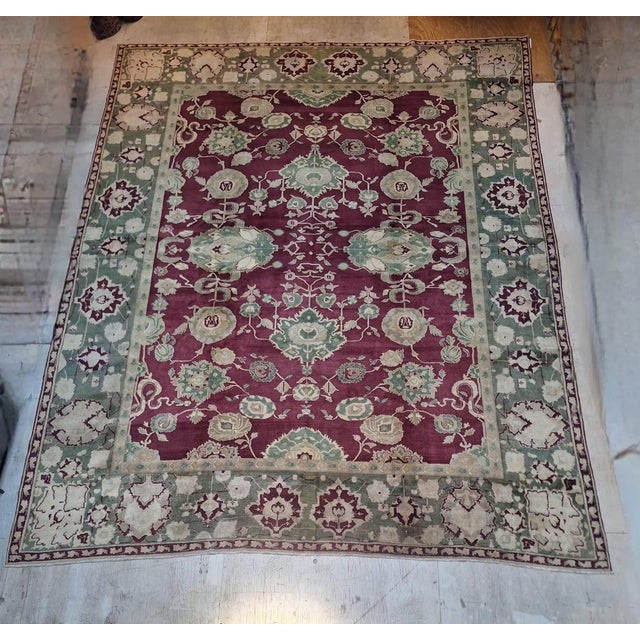0versized hand-knotted Indian Agra rug featuring a deep burgundy field framed by a soft sage green border. The rug...