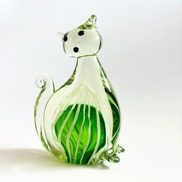A large vintage art glass cat. A green interior with white stripes is surrounded in clear glass. Measures 6"W x 2.5"D x...