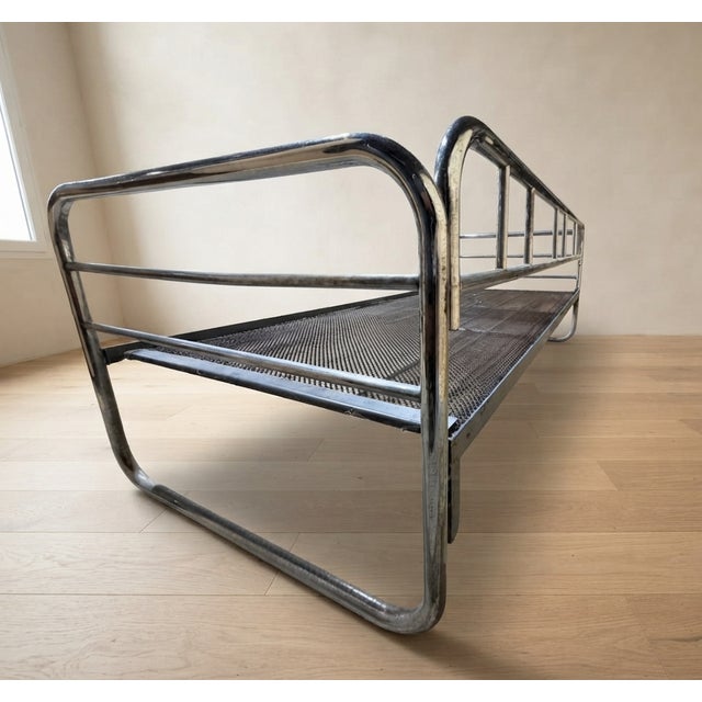 A distinctive vintage daybed frame featuring a chrome-plated tubular steel structure and woven metal mesh base. Its simple...
