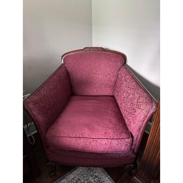 Victorian-era sofa and matching armchair featuring graceful carved wood frames, cabriole-style legs, and rich rose-colored...