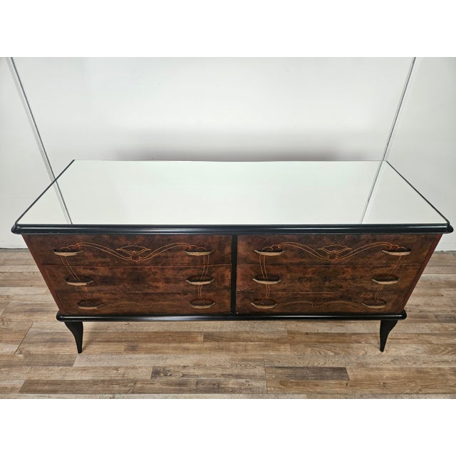 1960s chest of drawers clad in mahogany burl with brass trim and decorations. The mirrored top and black lacquered trim...