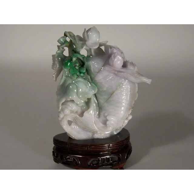 An eye catching multi-colored jade carving of a koi fish leaping from the water amongst a grouping of lotus plants. The...