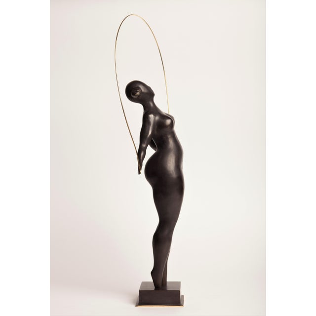 A contemporary figurative bronze of a standing woman with a skipping rope, the rope arching high overhead in a single...