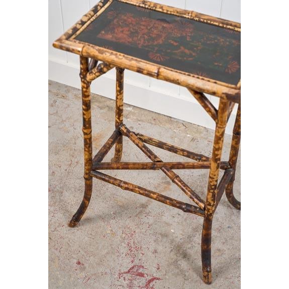 This 19th-century rectangular bamboo side table features a black lacquered top, framed by bamboo trim. The legs are gently...