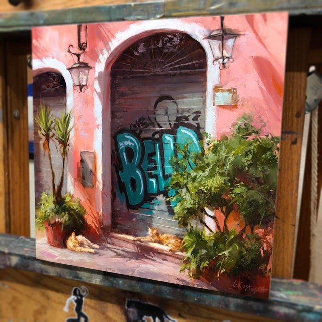 In "Riposa," a serene scene unfolds on a sunlit street, where two relaxed cats bask in the warmth near vibrant greenery...