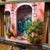 In "Riposa," a serene scene unfolds on a sunlit street, where two relaxed cats bask in the warmth near vibrant greenery...