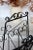 Elegant magazine rack in black lacquered metal, decorated with pretty wrought iron-style scrollwork. It features a central...