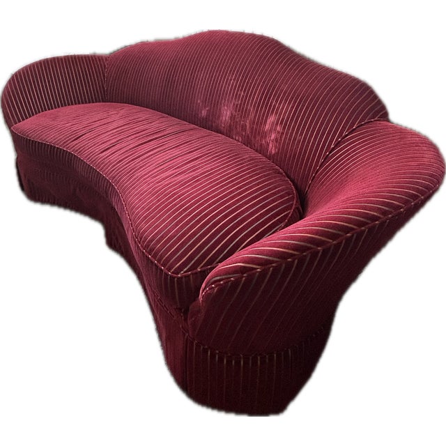 Cherry-red camelback curved banana sofa with tailored fringe skirt.