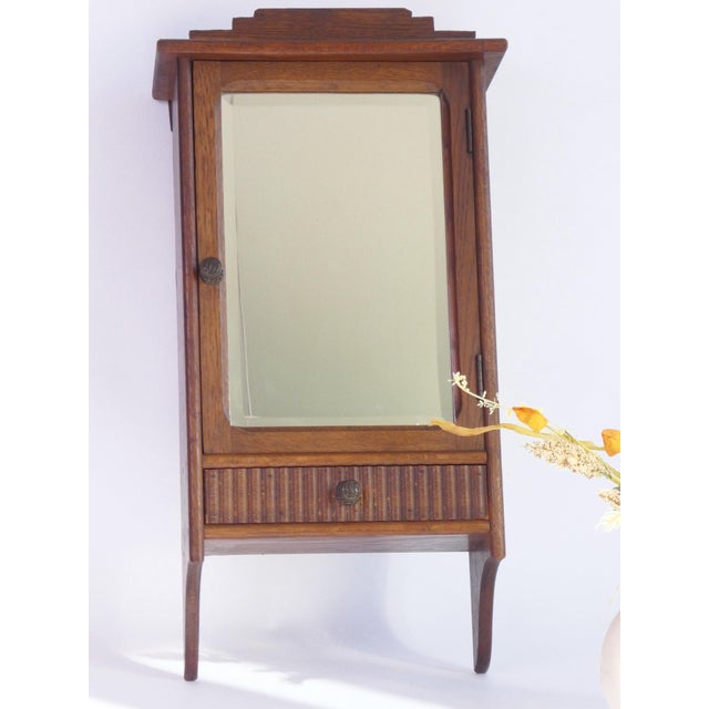 Antique wooden wall cabinet with a rectangular beveled mirror. The apothecary has a nice ornament on the top and the...