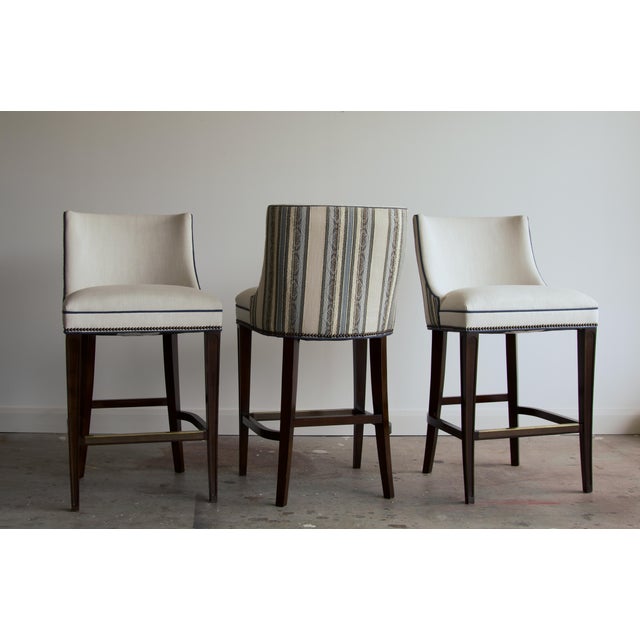 A set of three Wesley Hall bar stools in a custom two-tone treatment: cream linen on the inside back and seat, with a...