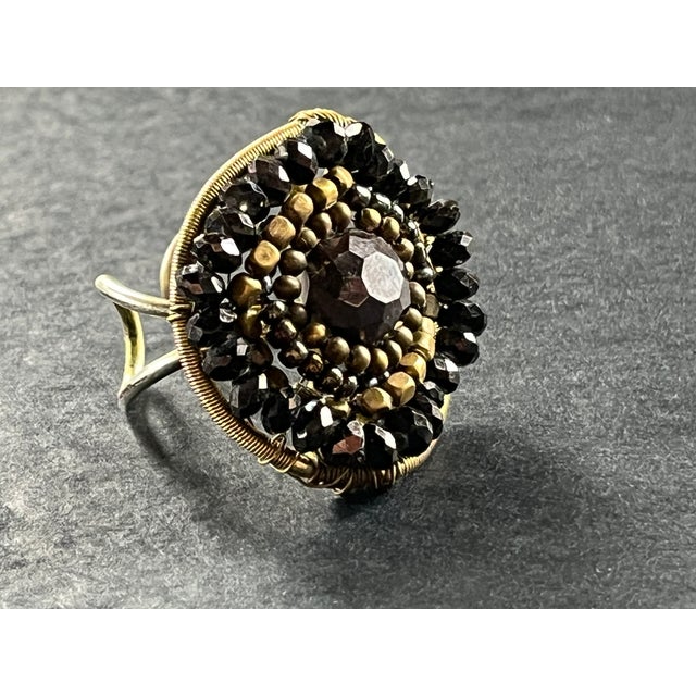 Hand‑assembled ring featuring concentric rows of faceted glass beads and metallic seed beads in black and antique gold...