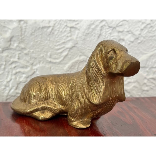 Solid brass figurine of a sitting spaniel. The dog has long feathered ears and a gently raised head. Fine cast brass...